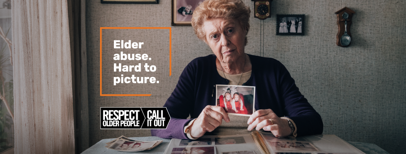 Older woman looking pensive, holding old family photograph of twin daughters