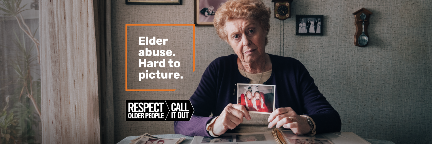 Older woman looking pensive, holding old family photograph of twin daughters, banner sized for twitter