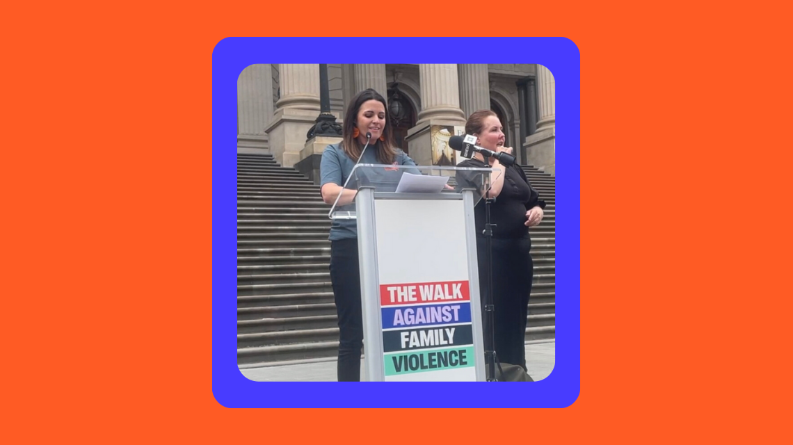 Professor Kate Fitz-Gibbon stands at a lectern that says "The Walk Against Family Violence". She on the steps of Victorian Parliament, addressing the 2023 Walk Against Family Violence. She is joined by an Auslan interpreter. 