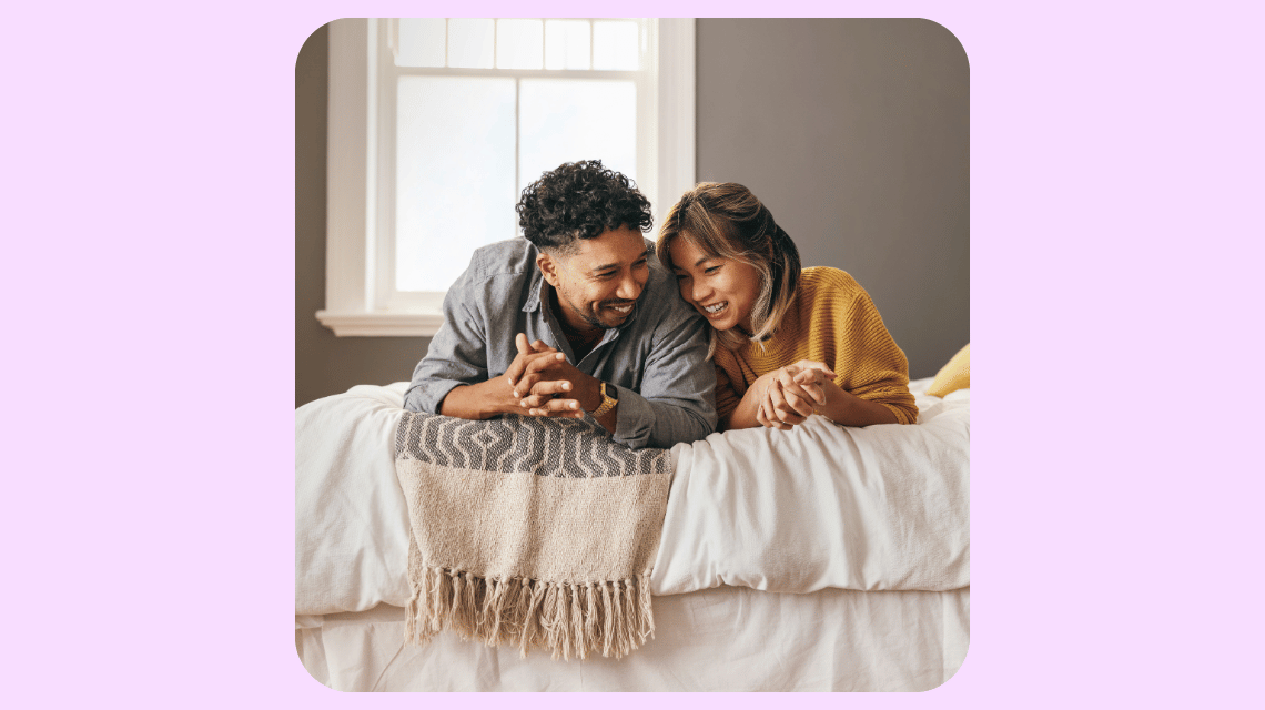 A man and woman lay on their stomachs on a bed, faced toward the camera.