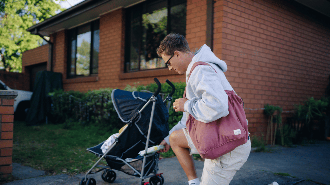 Adam, a What Kind of Man Do You Want to Be participant, kneels down to put baby wipes in the basket of a pram while out for a walk.