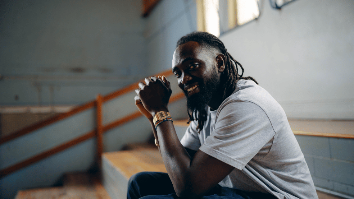 Mawout, a What Kind of Man Do You Want to Be participant, sits on bleachers at an indoor basketball court.