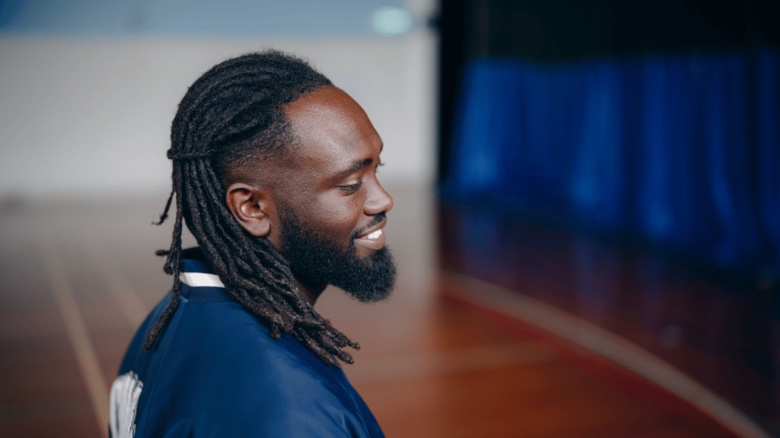 Mawout, a What Kind of Man Do You Want to Be participant, sits on bleachers at an indoor basketball court.