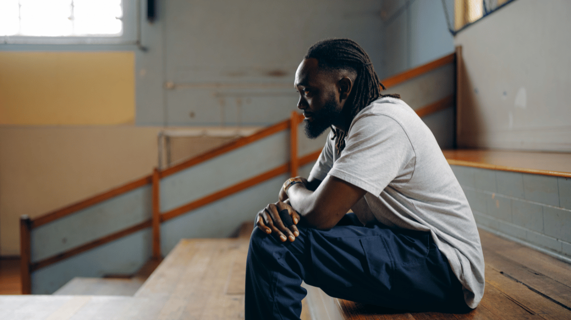 Mawout, a What Kind of Man Do You Want to Be participant, sits on bleachers at an indoor basketball court.