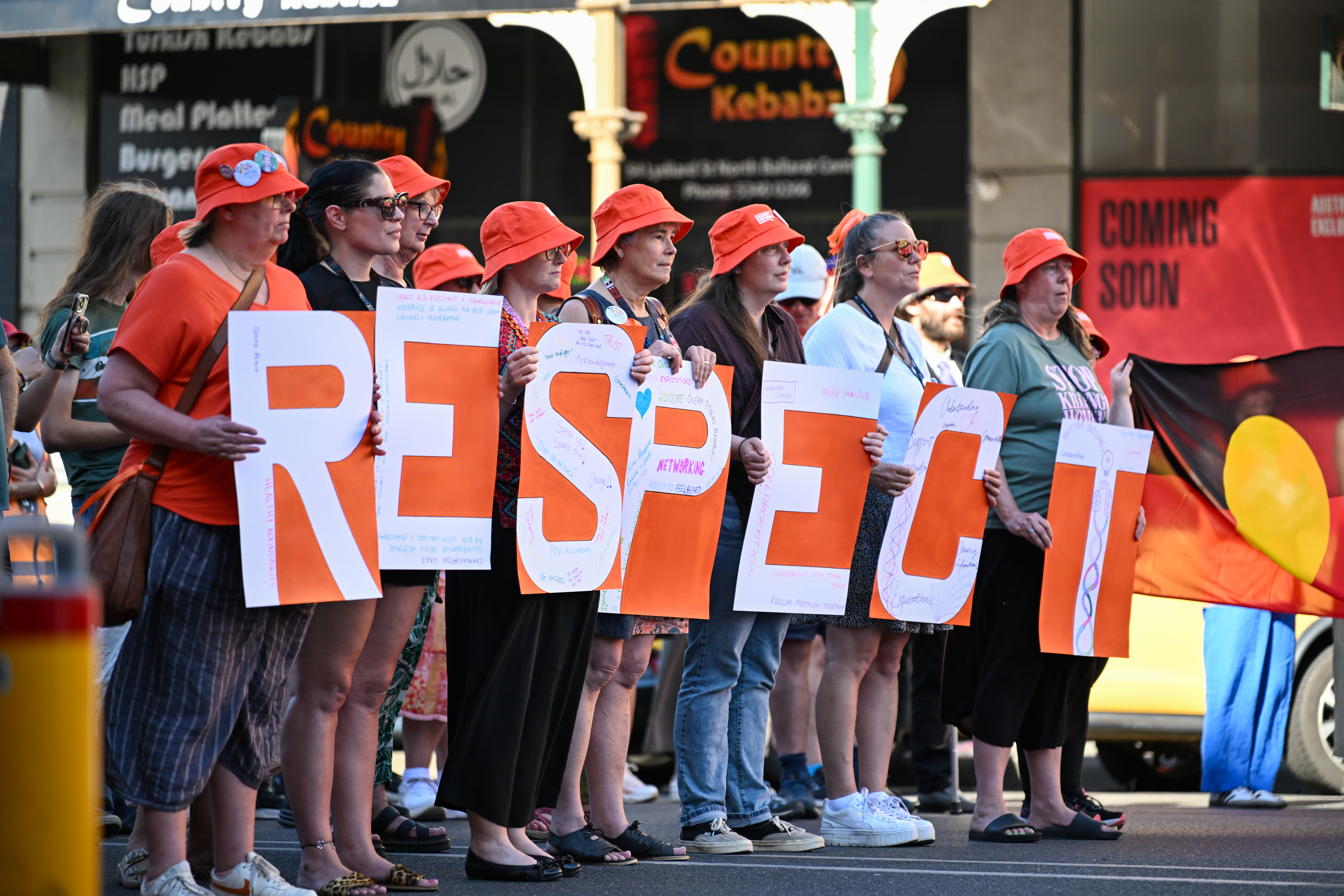 People stand together on the footpath holding up placards that spell out respect