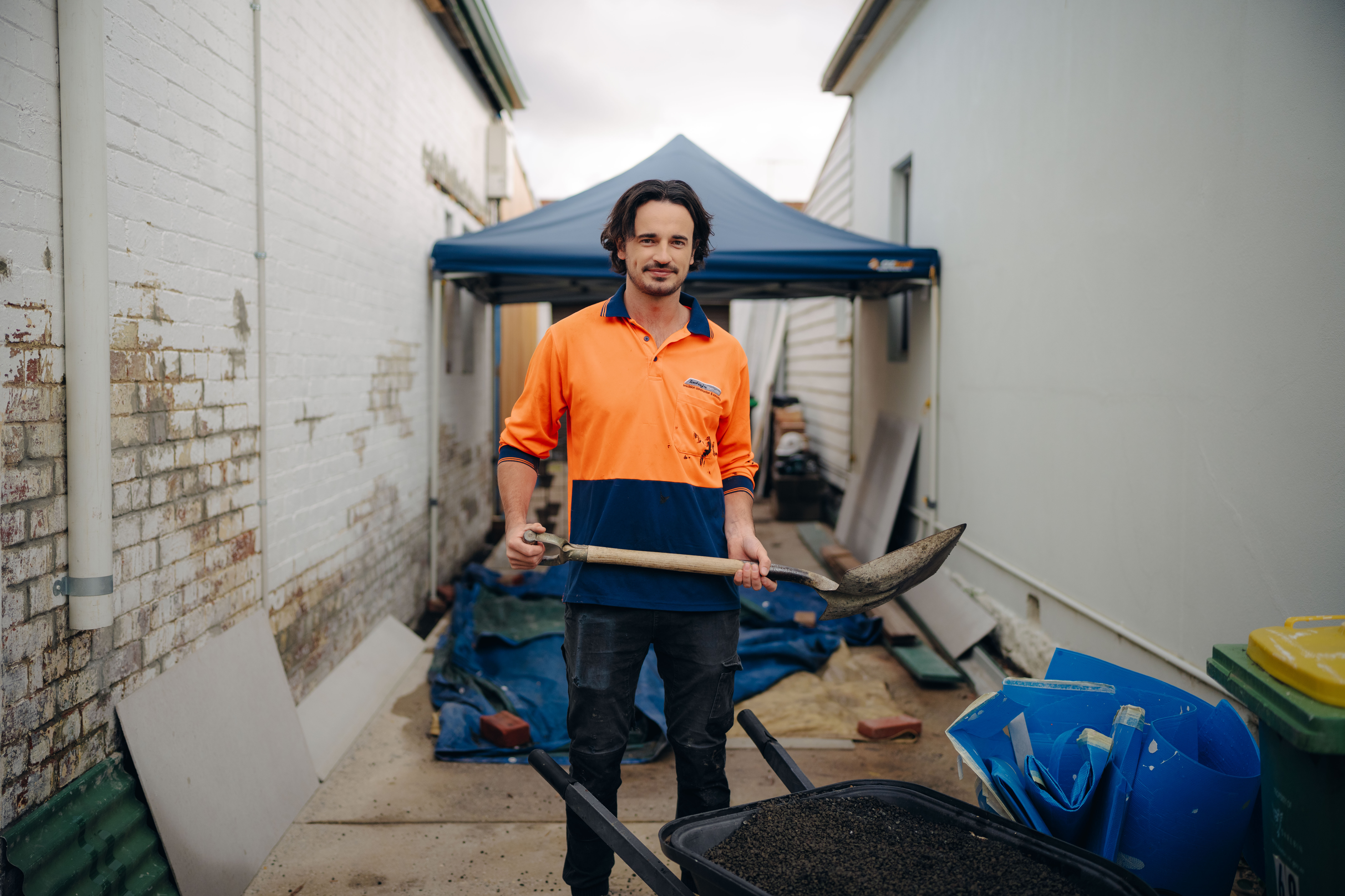 A male tradie wearing high vis gear holds a shovel on a domestic building site for the What Kind of Man Do You Want to Be? campaign.