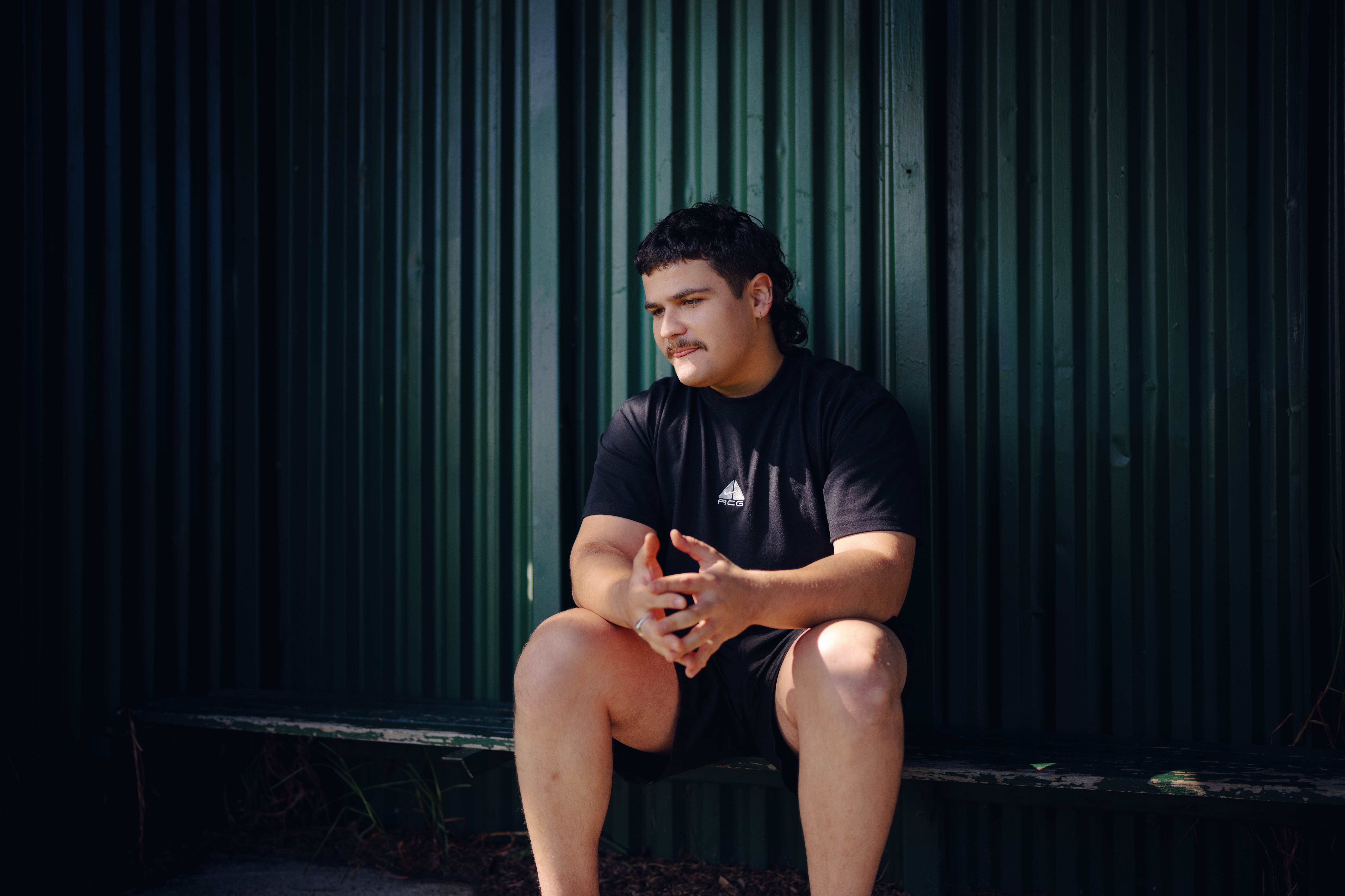 Young man sitting on green bench looking towards the distance for the What Kind of Man Do You Want to Be? campaign.