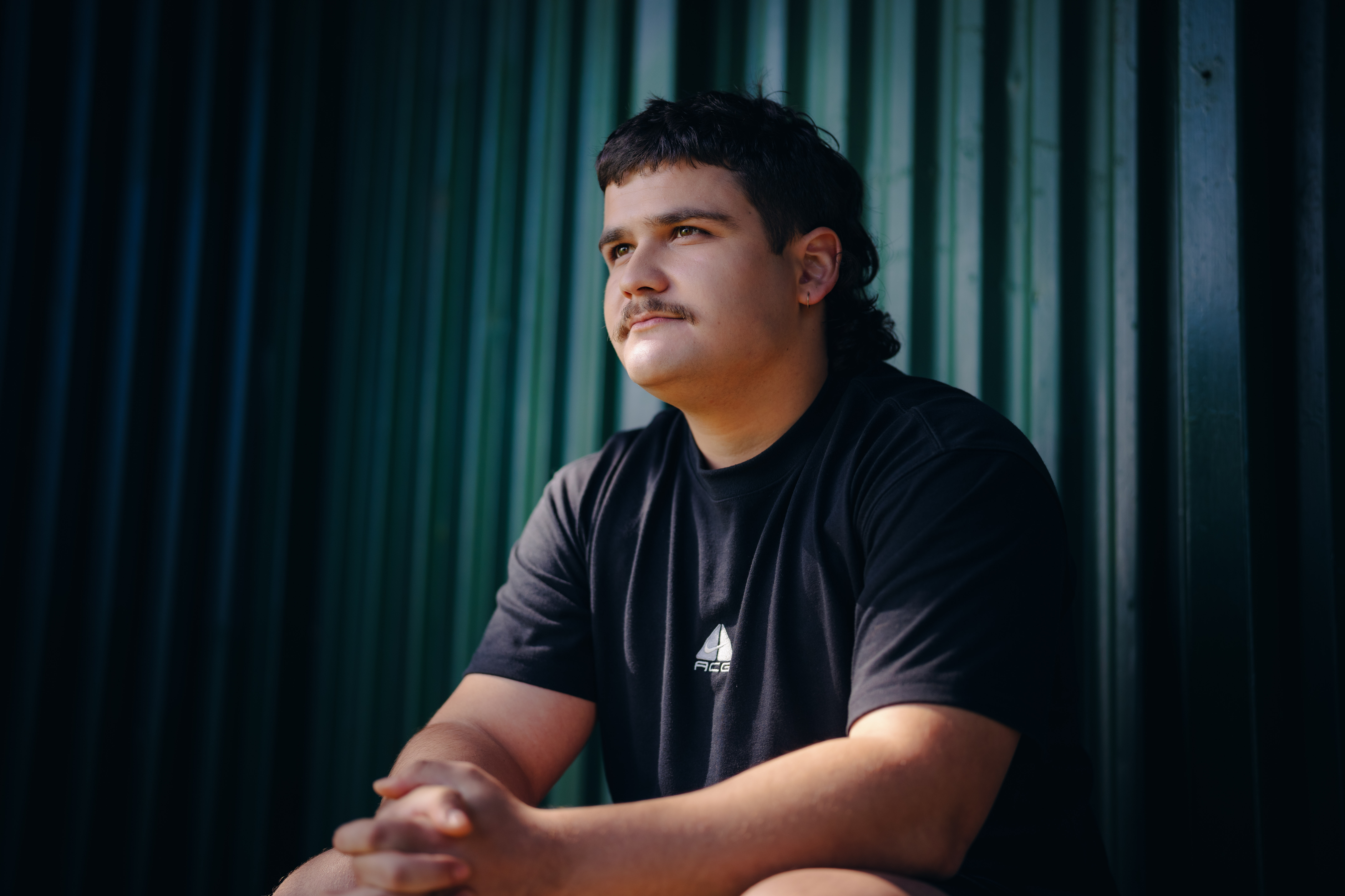 Young man sits on green bench looking towards distance for the What Kind of Man Do You Want to Be? campaign.