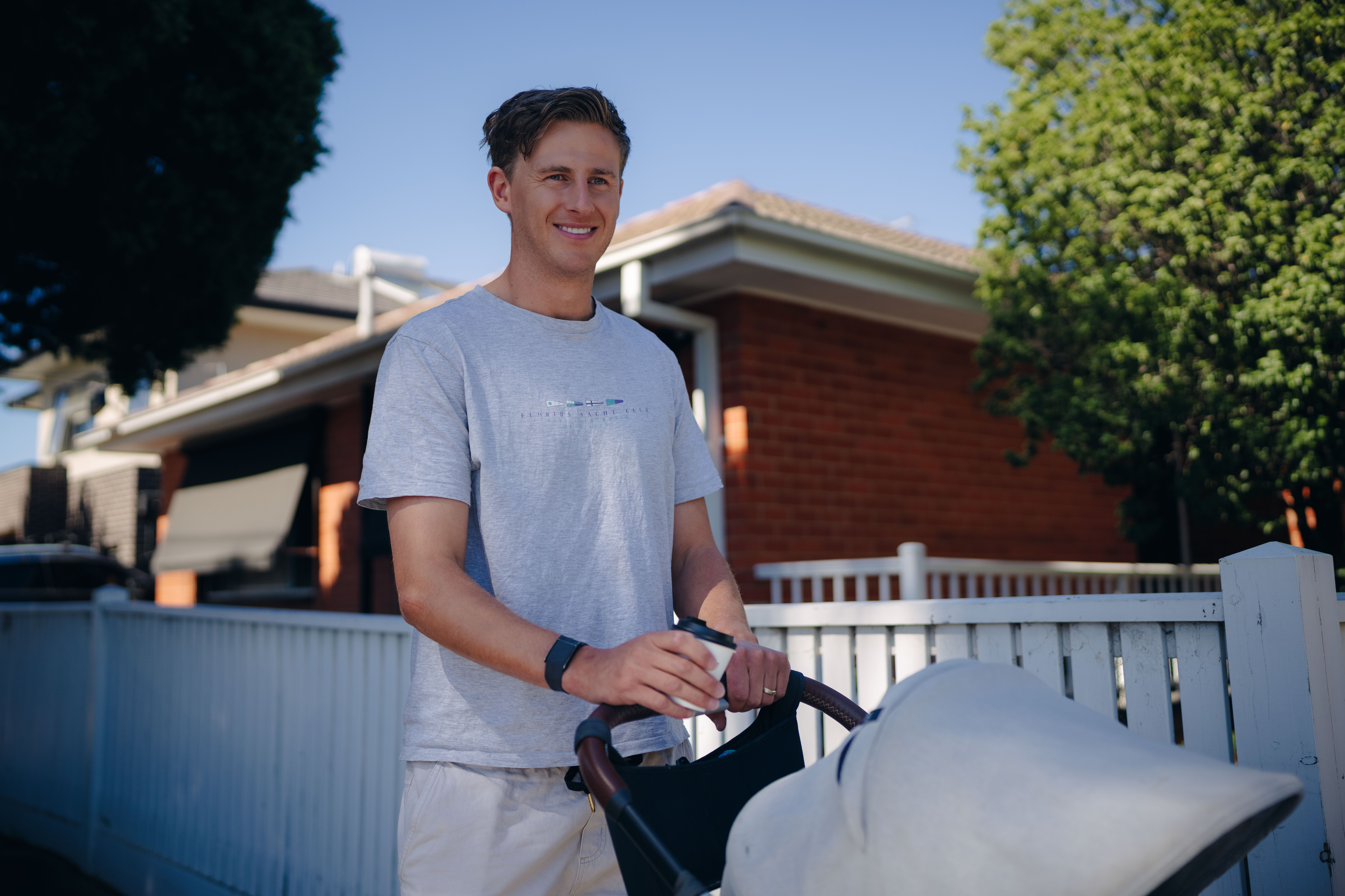 Young father wearing grey t-shirt pushes baby in pram along suburban street