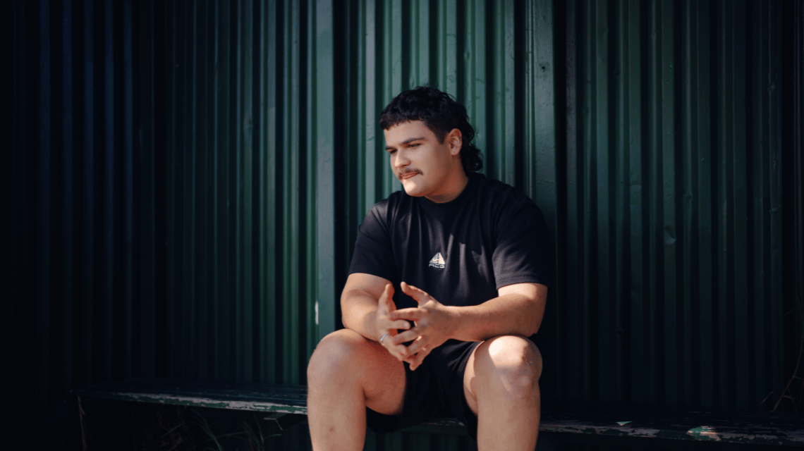 Young man sitting on green bench looking towards the distance for the What Kind of Man Do You Want to Be? campaign.