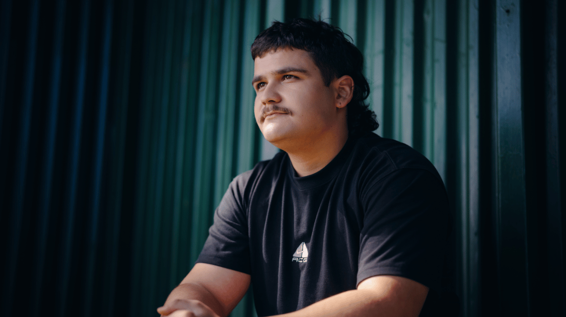 Young man sitting on a bench, hands clasped on his knees, gazing into the distance.