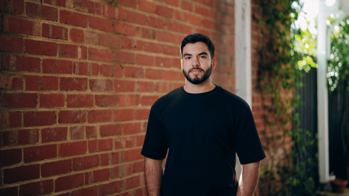 Portrait of a man in a black t-shirt standing in front of a brick wall