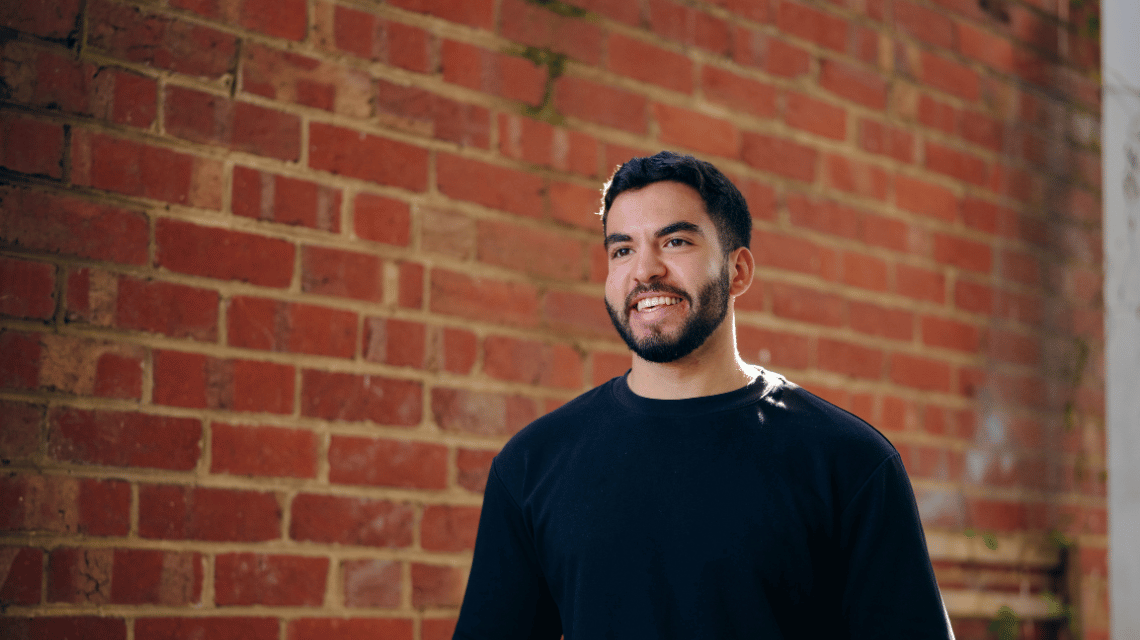 Portrait of a smiling man in a black t-shirt standing in front of a brick wall