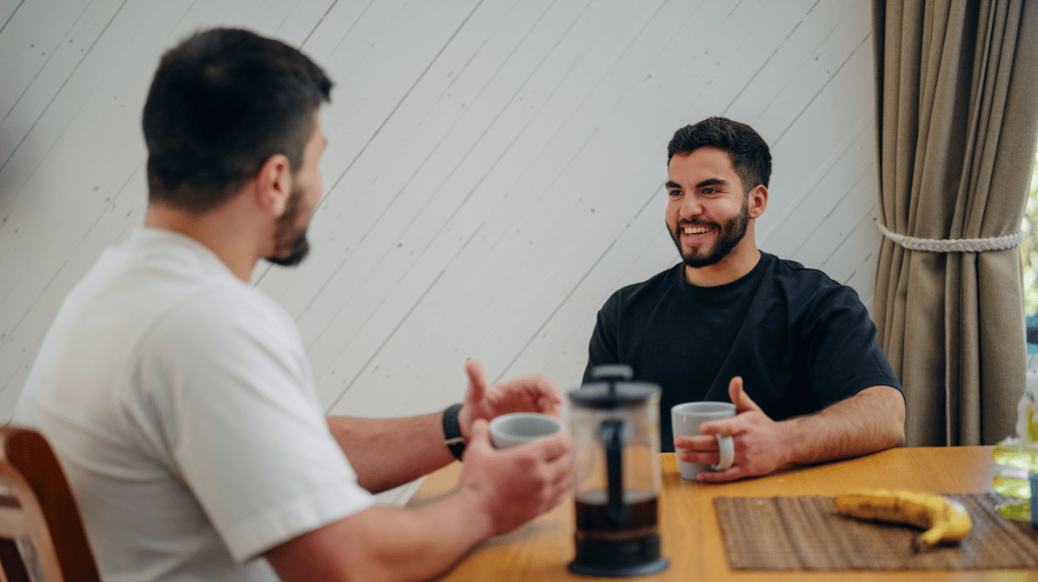 Two men drink coffee at a kitchen table and chat.