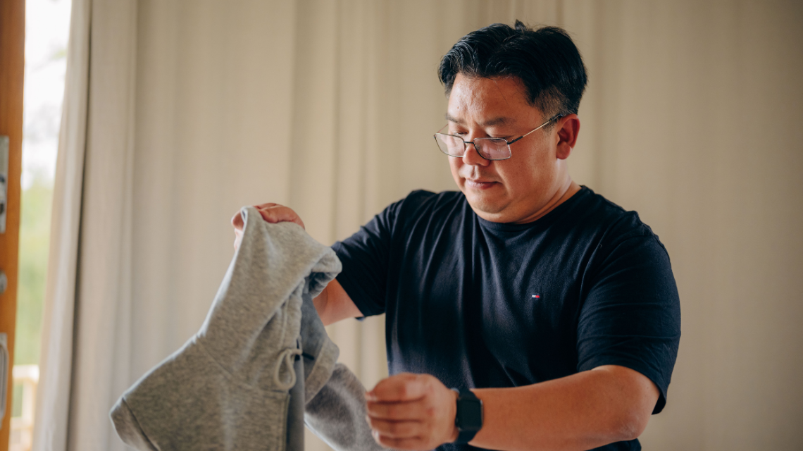 A man in a black t-shirt folds laundry.