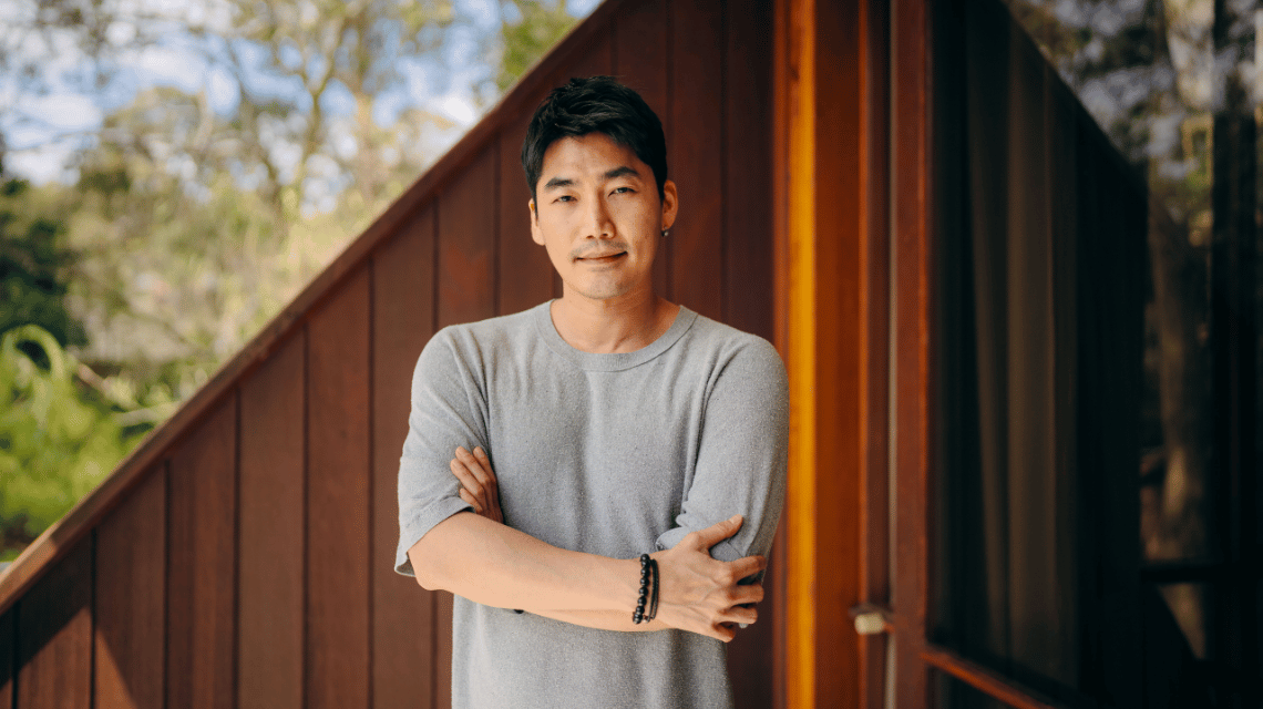 Portrait of a man in a grey t-shirt, standing on a home balcony.