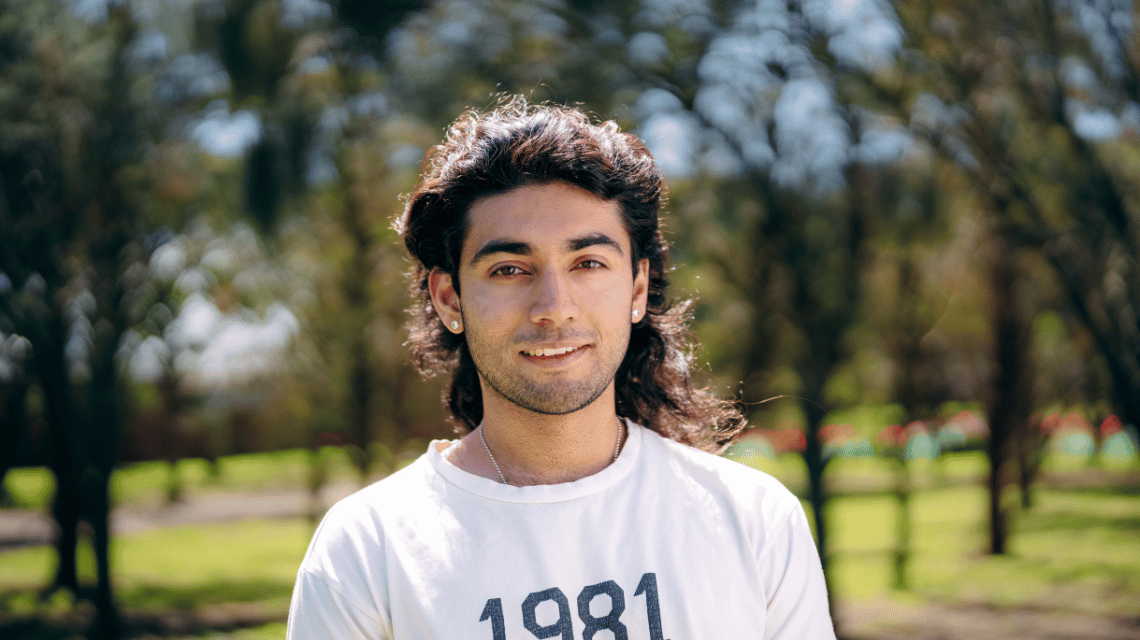 Portrait of a man in a white t-shirt outside, long black hair swept back by wind
