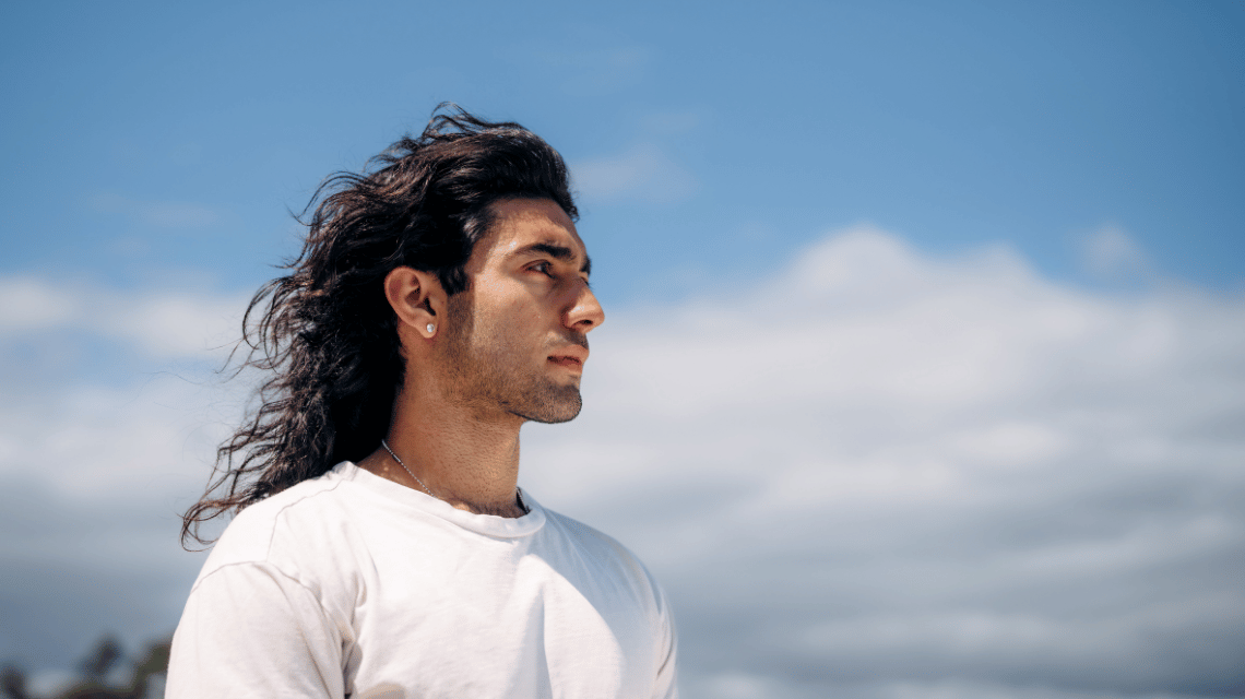 Portrait of a man in a white t-shirt outside, long black hair swept back by wind