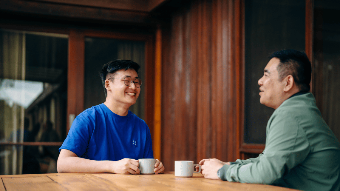 Two men sit on a home balcony and drink tea.