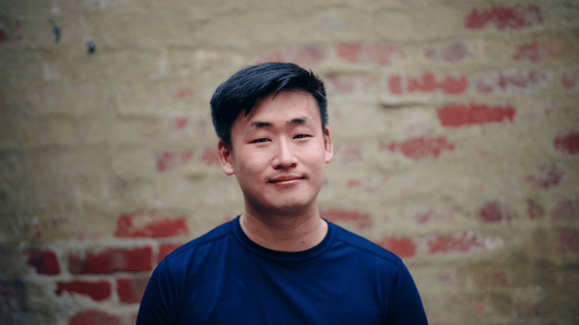 Portrait of a man in a blue sweater, standing in front of a brick wall