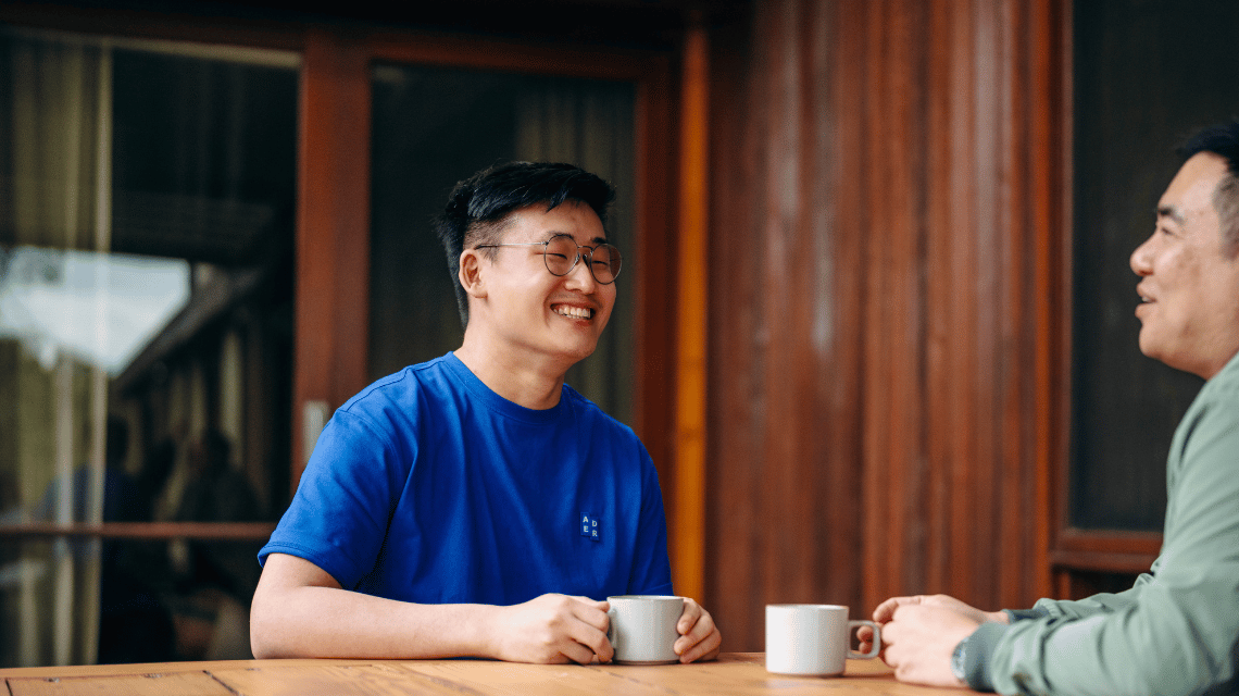 A man in a blue t-shirt drinks tea with a friend.