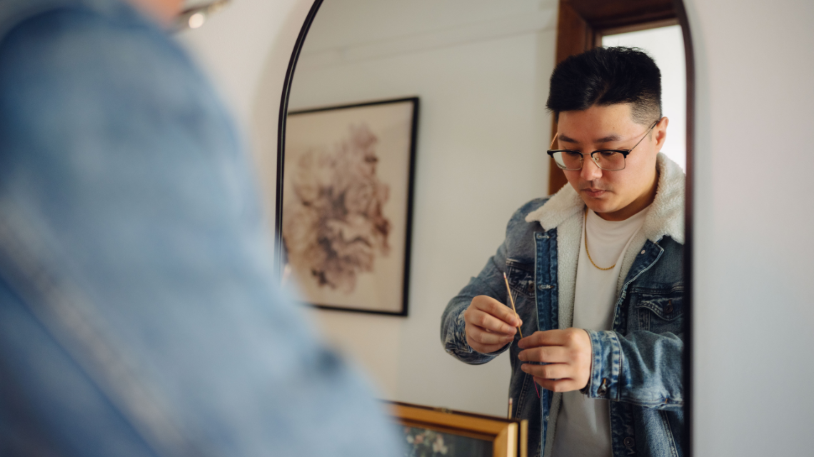 Reflected in a mirror, a man lights incense.