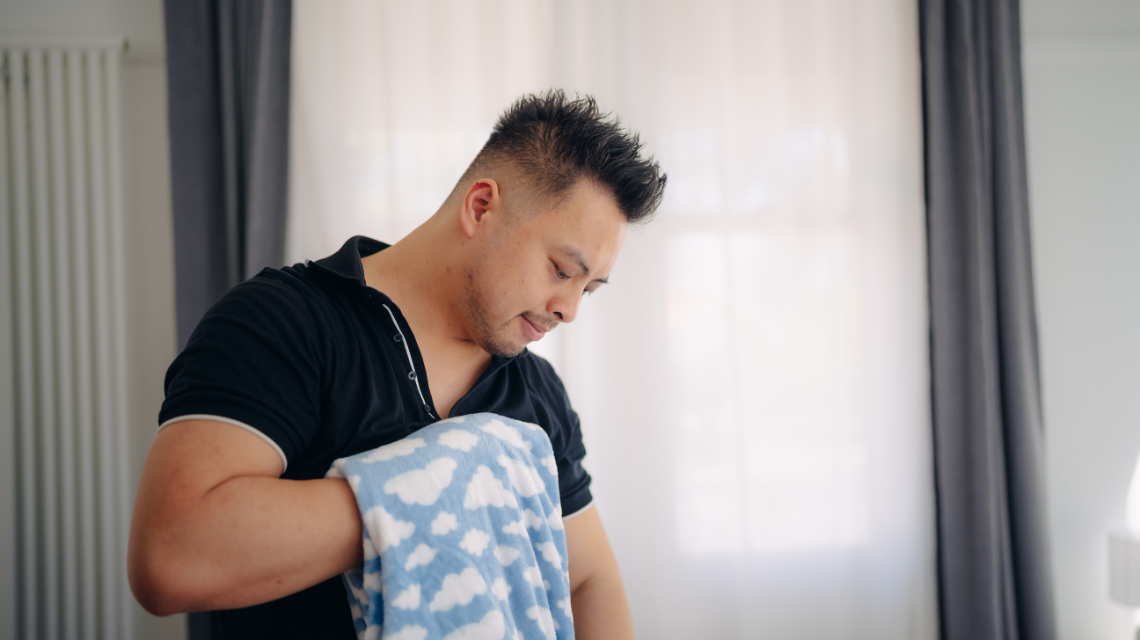 A man in a black t-shirt folds laundry.