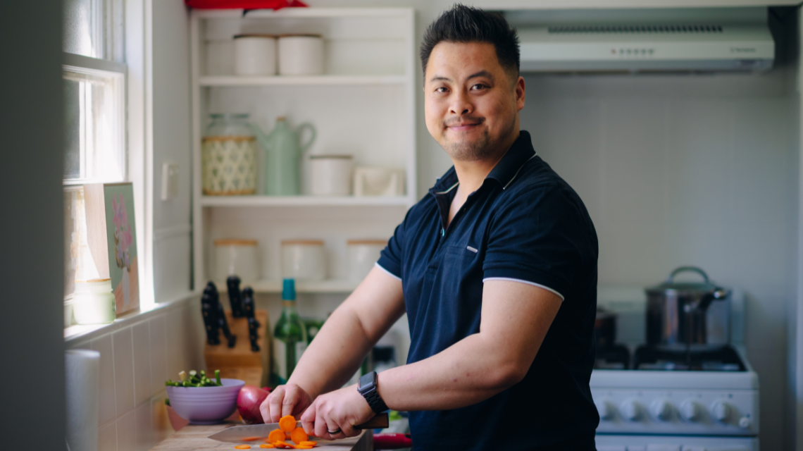 A man prepares vegetables in a home kitchen. He smiles at the camera. 