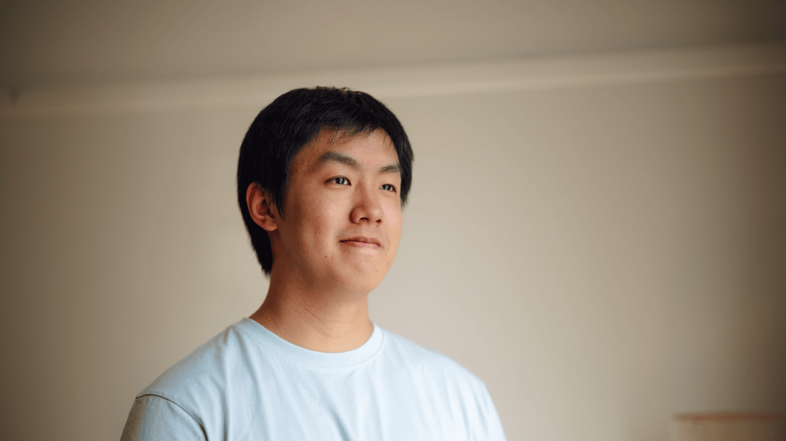 A portrait of a man in a white t-shirt, looking thoughtfully off camera.