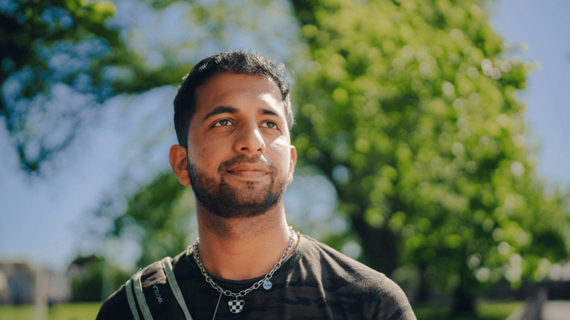 A man in a grey t-shirt looks thoughtfully in a park.