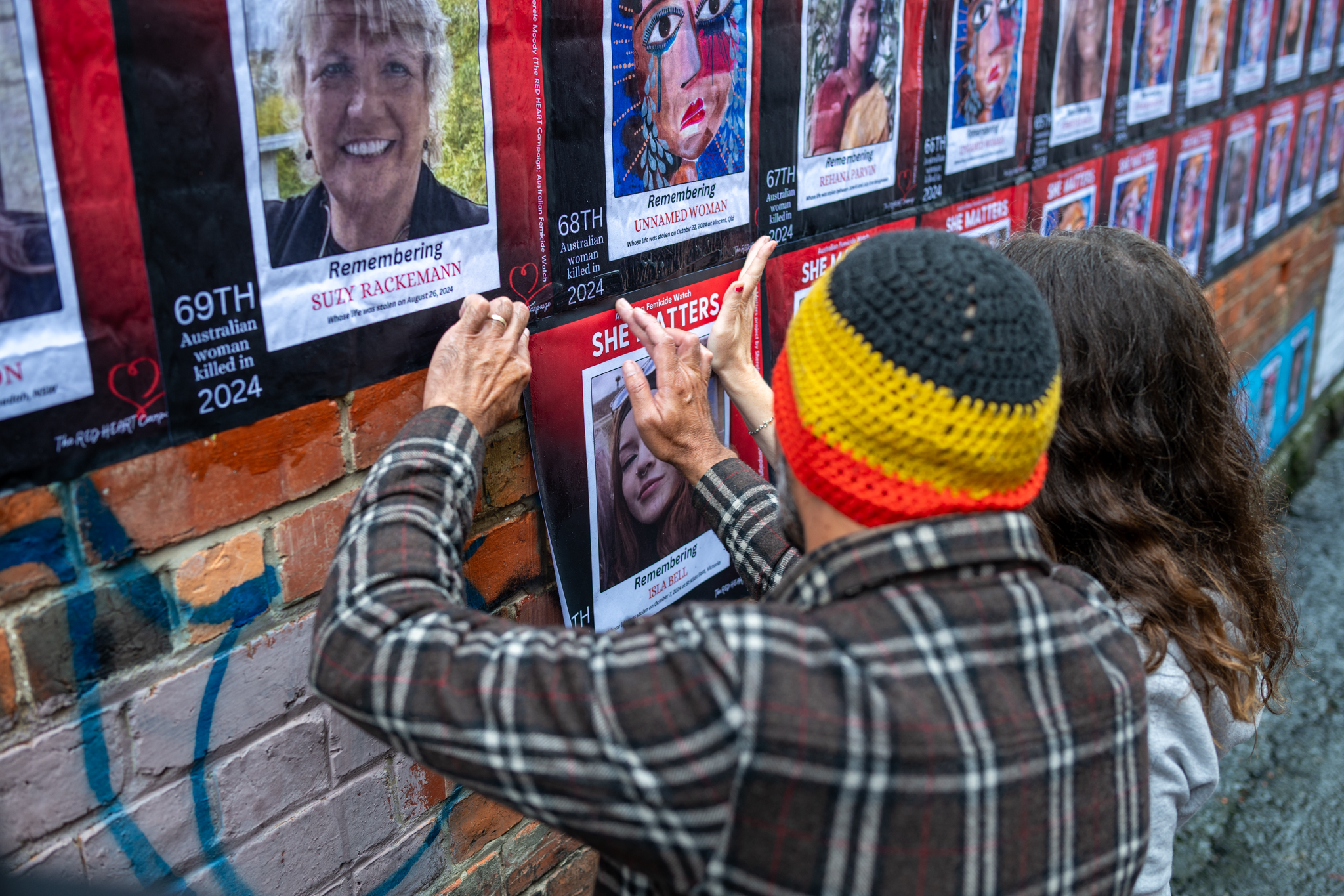 Two people install a photograph of Isla Bell on the mural