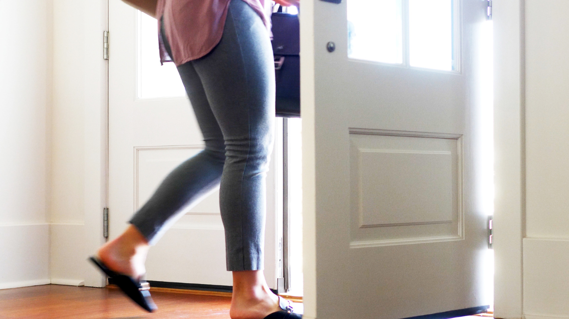 From the hips down, a woman is walking out of a residential front door.